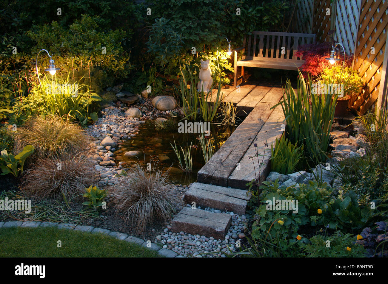 Am frühen Abend britischen Garten im Sommer, verfügt über einen Teich, Gartenstuhl, Lichter und Stein Detail. Stockfoto