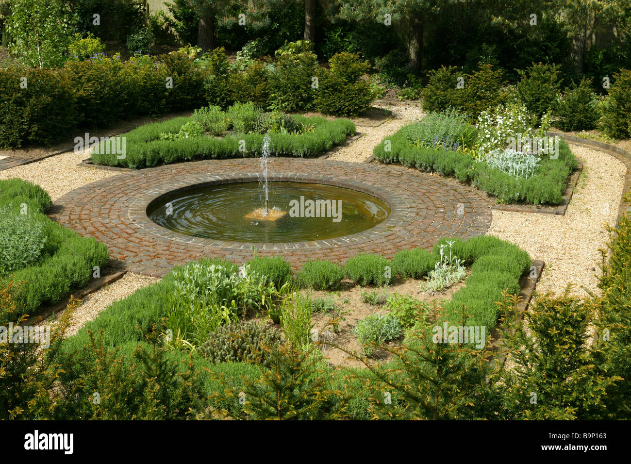 Englischen Landschaftsgarten angelegt mit Kies und Grenzen und eine zentrale Wassereigenschaft eines kreisförmigen Brunnens. Stockfoto