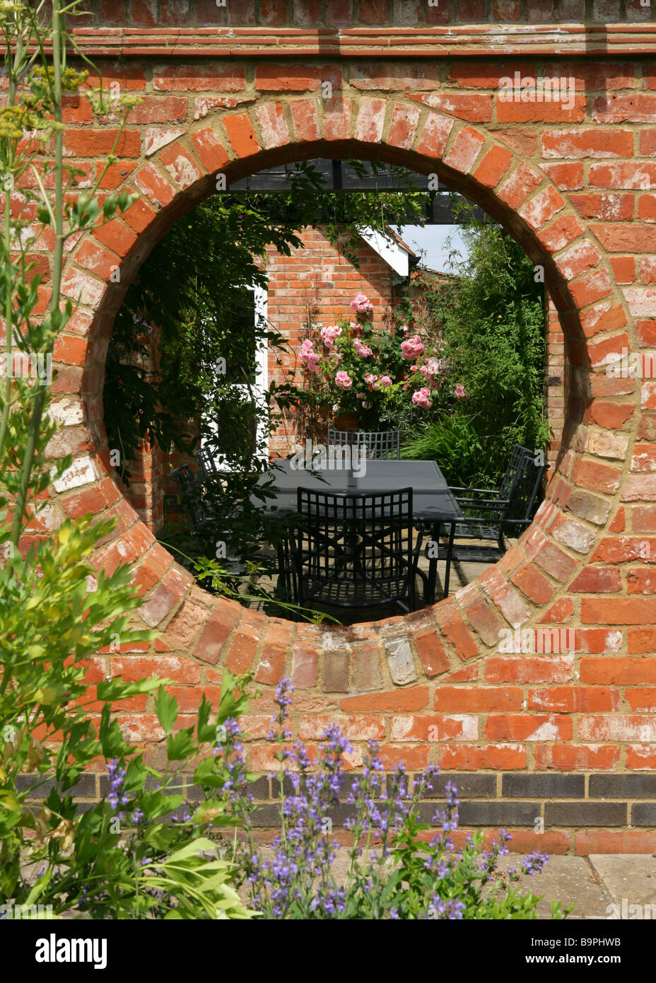 Blick in einen ummauerten Garten durch Kreisloch in Terrcotta Ziegelmauer, England. Stockfoto