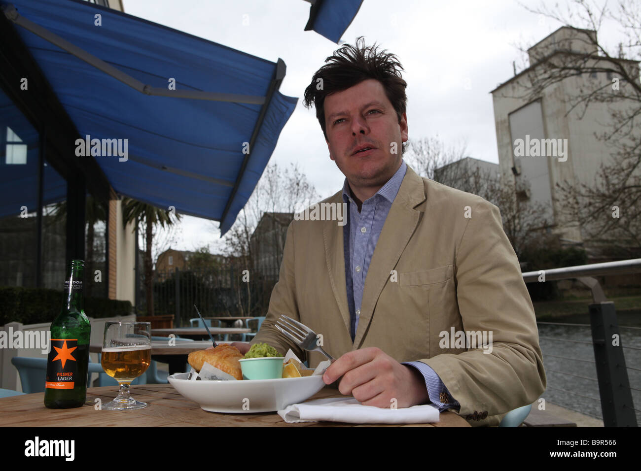 ein Porträt von ein kluger Mann vor einem Restaurant Essen Fish &amp; Chips neben einem Kanal mit einem Bier in der Sonne sitzen Stockfoto