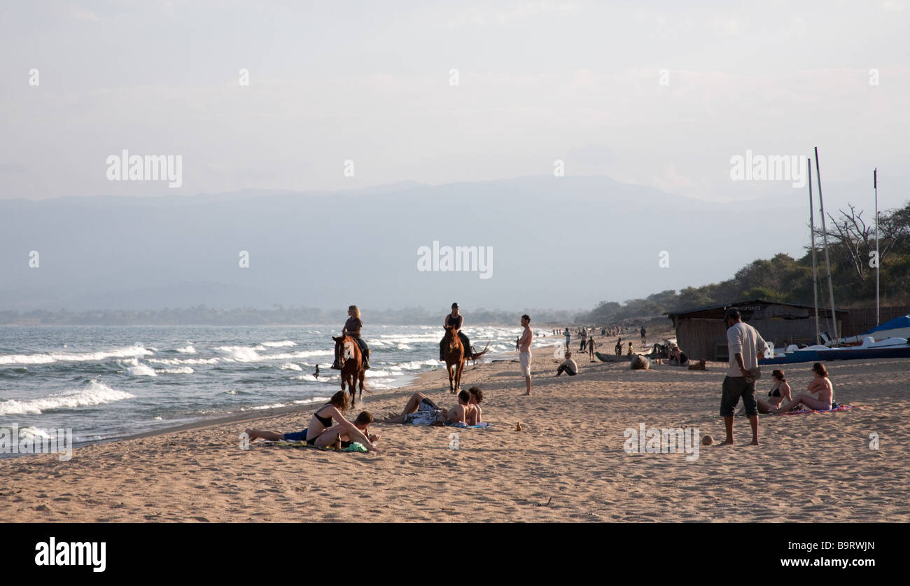 Europäer am Kande Beach von Malawi-See, während einige einheimische Kinder schwimmen und spielen. Stockfoto