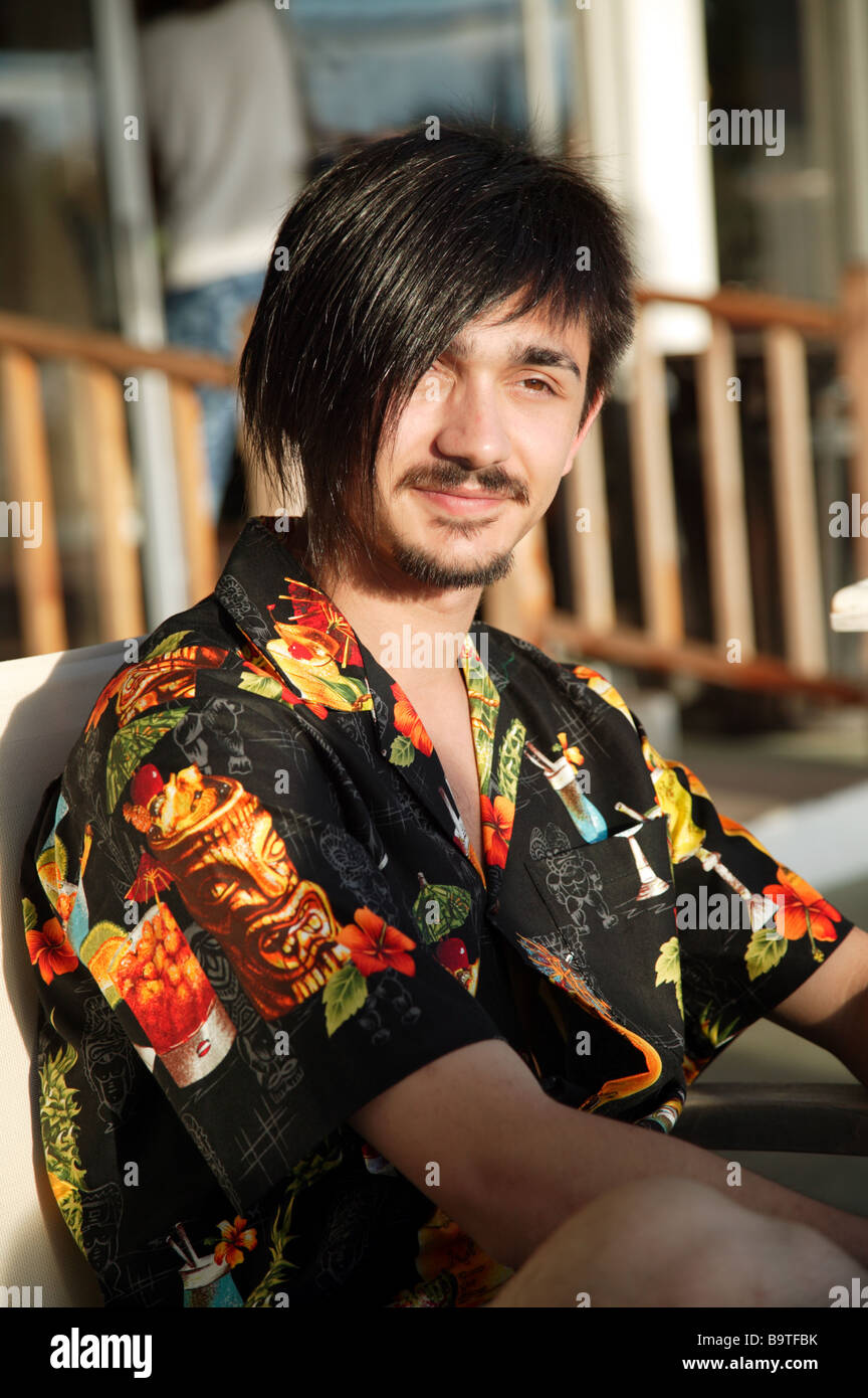 Nahaufnahme eines sitzenden lächelnden jungen Mannes tragen ein Hawaii-Hemd Stockfoto