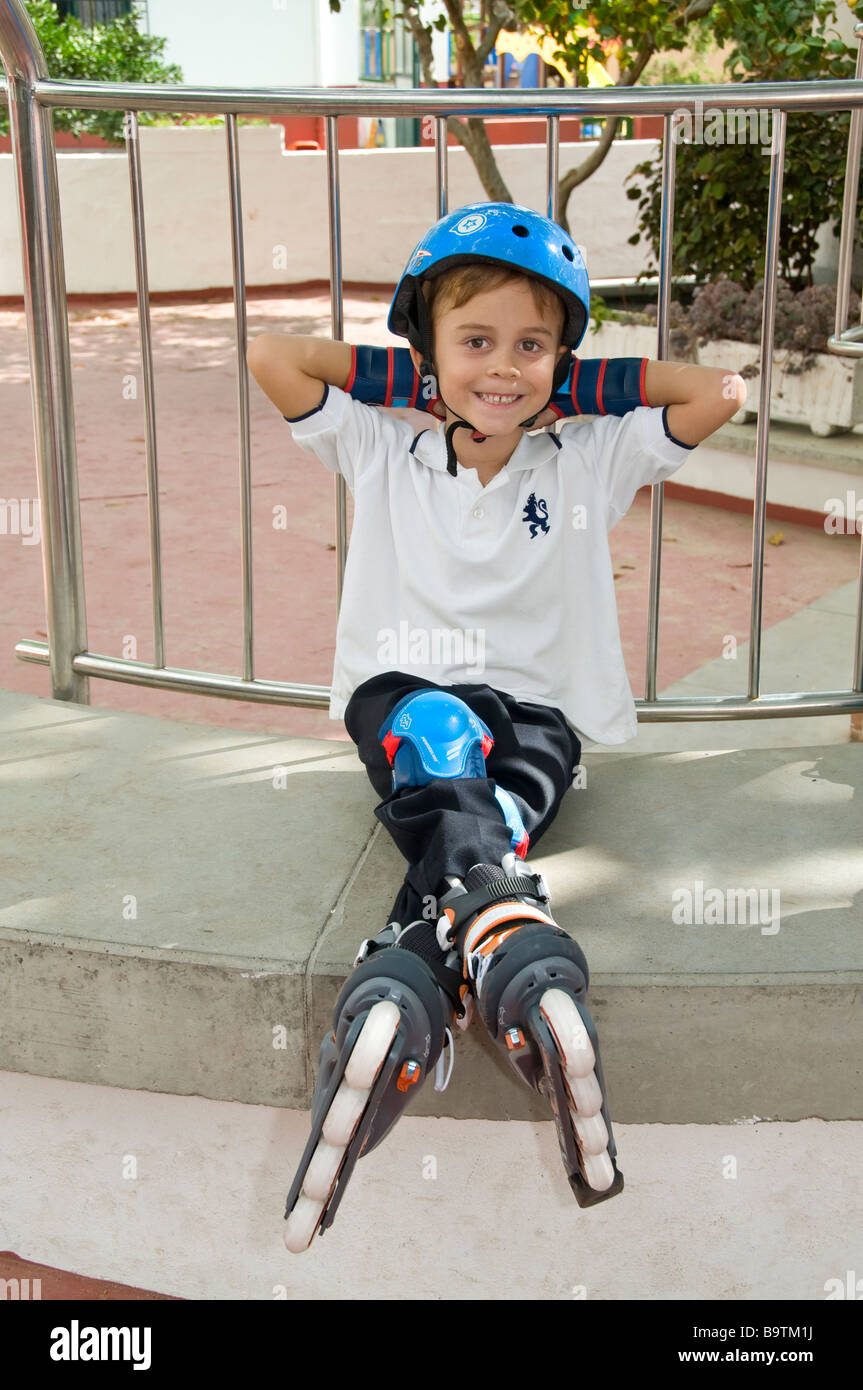 Junior Schüler sitzen und entspannen auf dem Spielplatz Campus Rollerblade Schutzkleidung tragen Stockfoto
