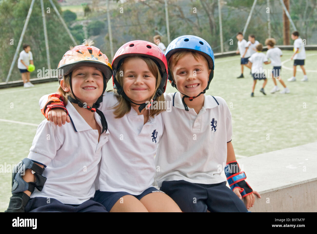 Happy junior School Kinder sitzen auf Wand tragen Schutzhelme Sport im Sport Spielplatz Schulcampus Stockfoto