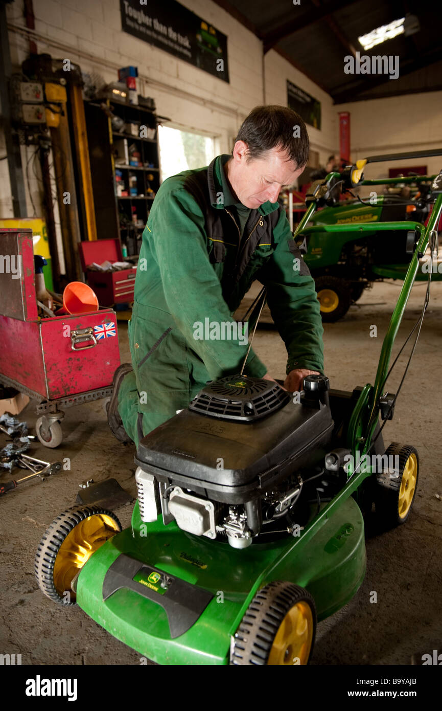 Ein Techniker tragen grüne Overalls Reparatur John Deere Rasenmäher in der Garage-Werkstatt, UK Stockfoto