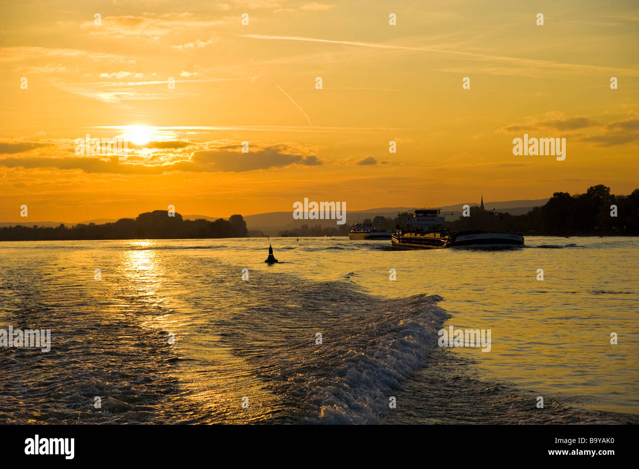 Motorboot Gefolge und Cargo Schiffen im Sonnenuntergang am Rhein | Deutschland Heckwelle Eines Motorbootes Und Frachtschiffe Auf Den Rhein Stockfoto