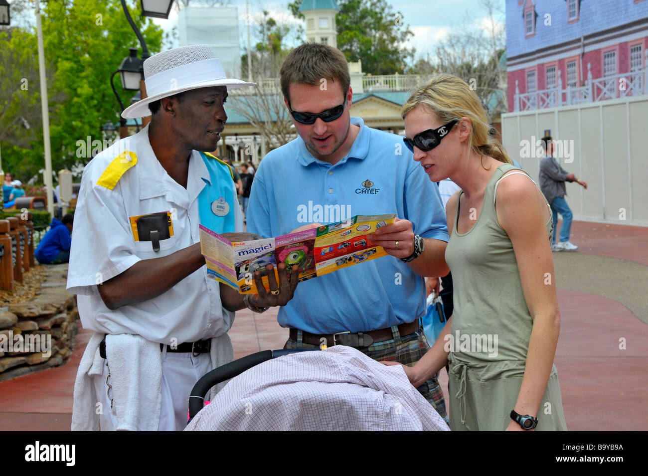 African American male Reiseführer hilft weiße junges Paar mit Kind und Kinderwagen Blick auf Karte Disney Magic Kingdom Orlando Florida Stockfoto