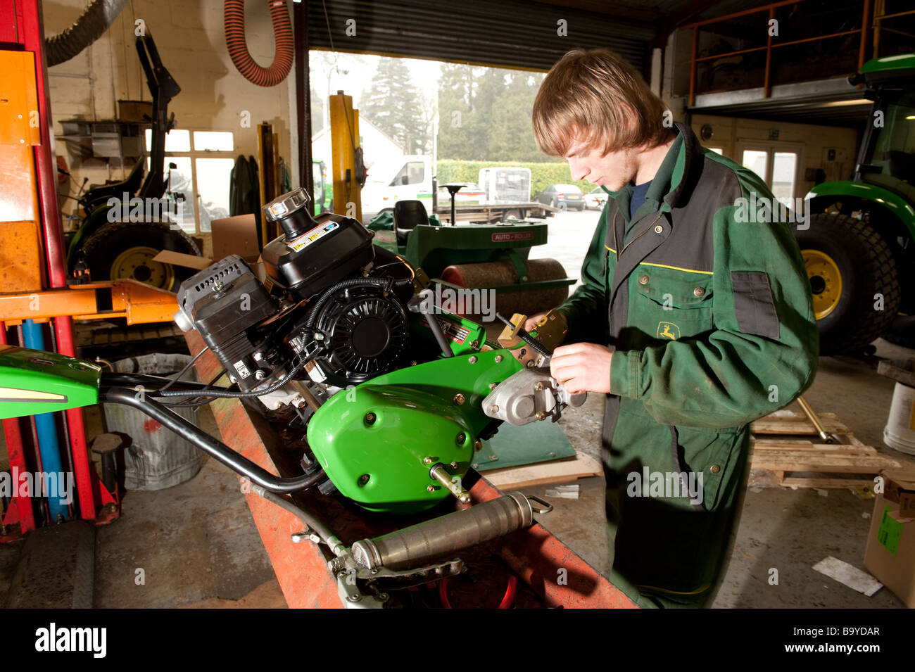 Ein junger Lehrling tragen Overalls Overalls arbeiten auf die Reparatur von eines John Deere Rasenmähers in der Garage-Werkstatt, UK Stockfoto