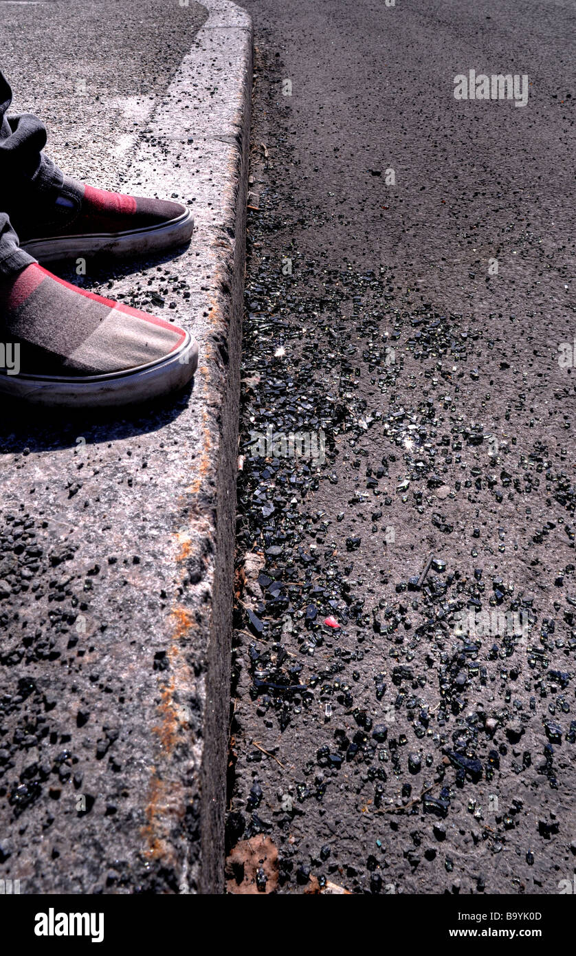 Hipster mit Tartan Schuhe auf dem Bordstein mit kaputten Auto Fensterglas und Schutt zu seinen Füßen stehen. Bilder des Verfalls des urbanen Lebens Stockfoto