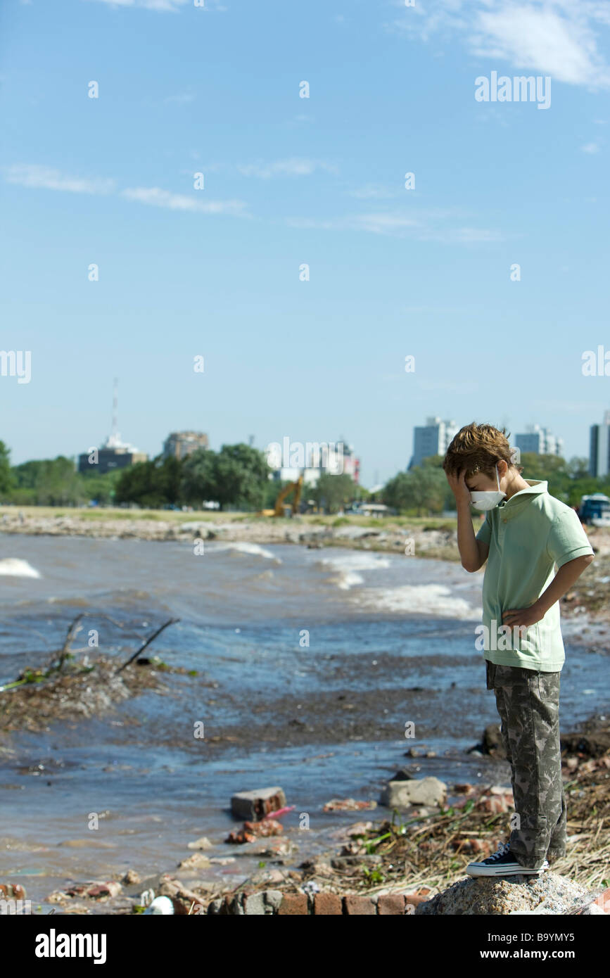 Junge stand auf verschmutzten Ufer, mit Umweltverschmutzung Maske, Kopf nach unten Stockfoto