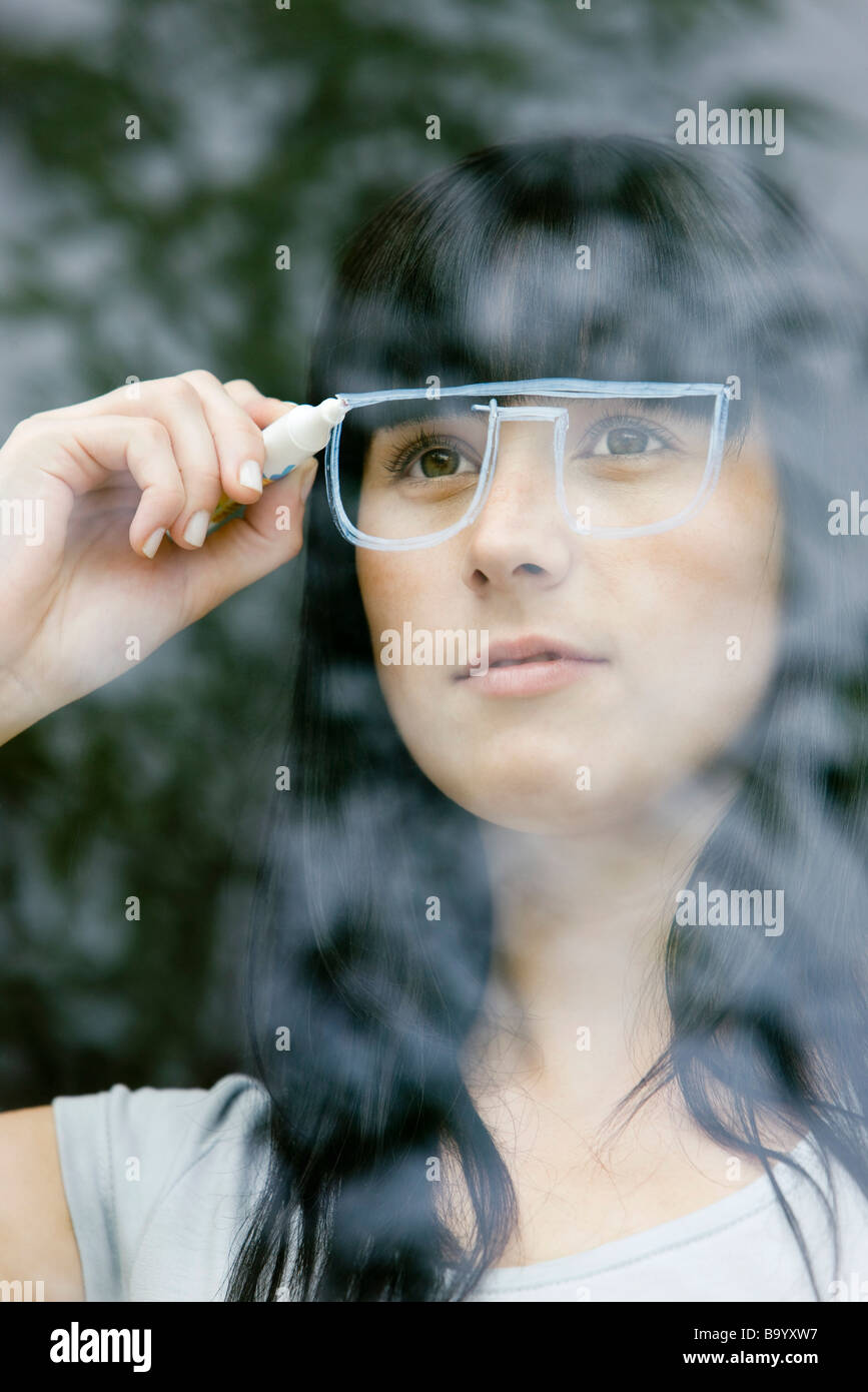 Junge Frau zeichnen ein paar Gläser auf einer Fensterscheibe, Blick durch Fenster Stockfoto