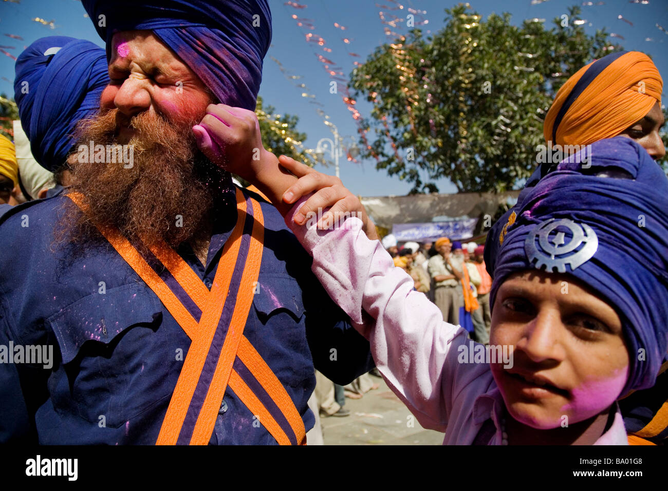 Ein junger Nihang/Akali/Sikh wendet Farbe auf seines Vaters Gesicht während des Festivals von Holla Mohalla an Anandpur Saheb, Punjab, Indien Stockfoto
