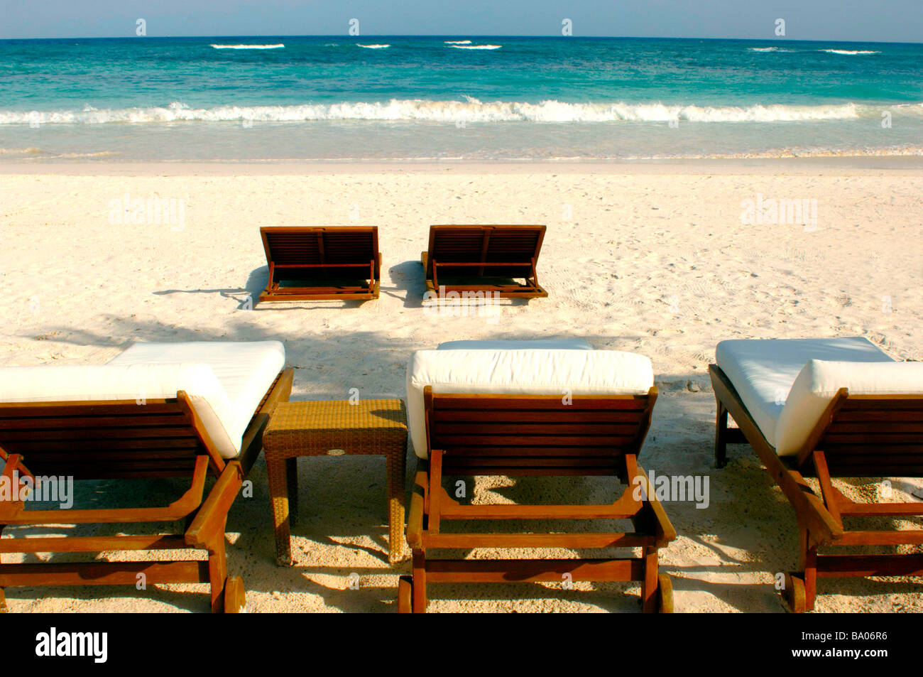 Liegestühle und Schirme an einem tropischen Strand mit schönen weißen Sand, blaues Wasser und brechenden Wellen. Stockfoto