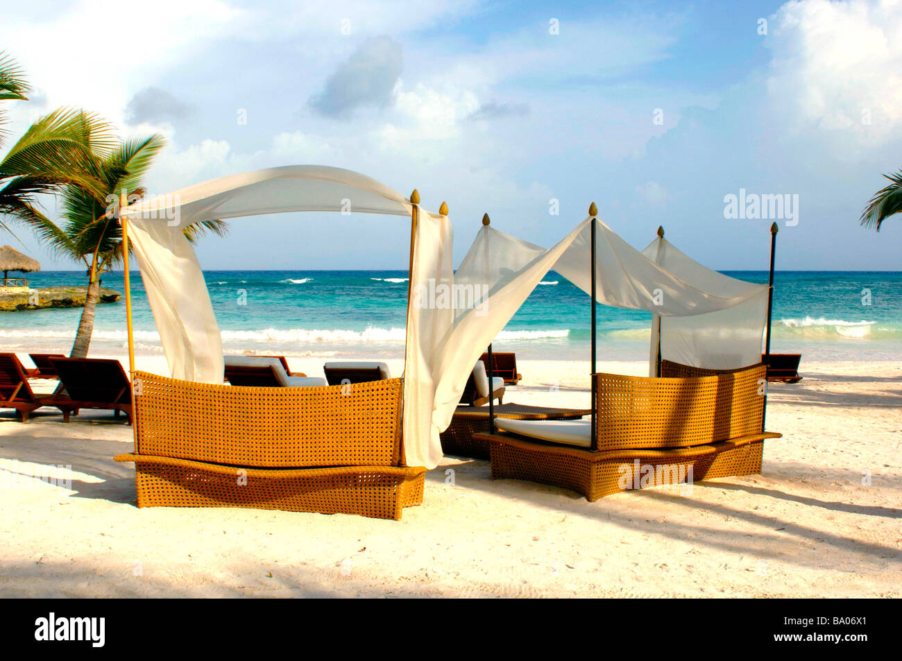 Liegestühle und Schirme an einem tropischen Strand mit schönen weißen Sand, blaues Wasser und brechenden Wellen. Stockfoto