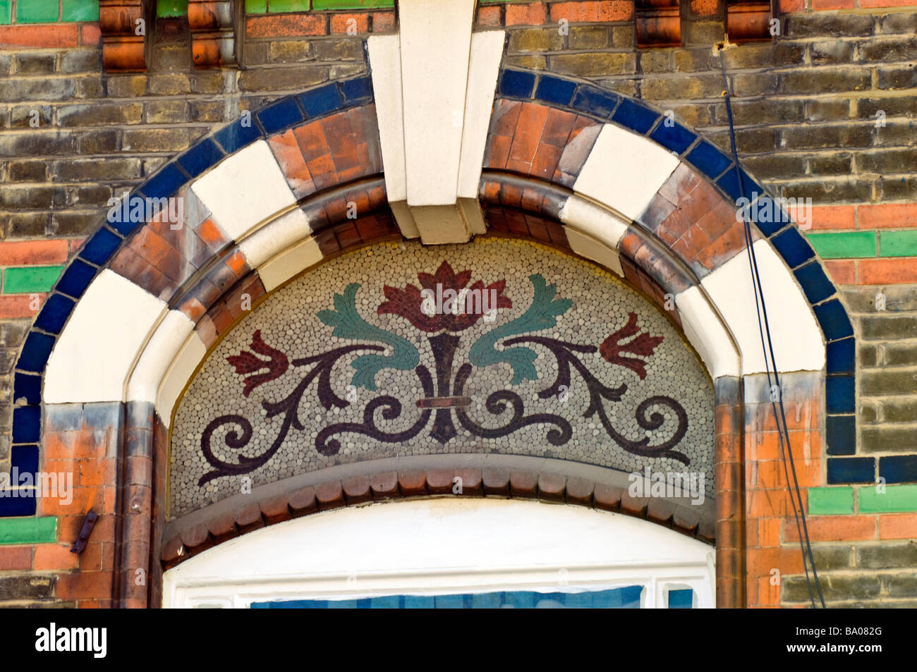 Bunt bemalten Fenster Bogen und architektonische Detail von einem Blumenmotiv als ein Mosaik auf ein Gebäude, London. Stockfoto