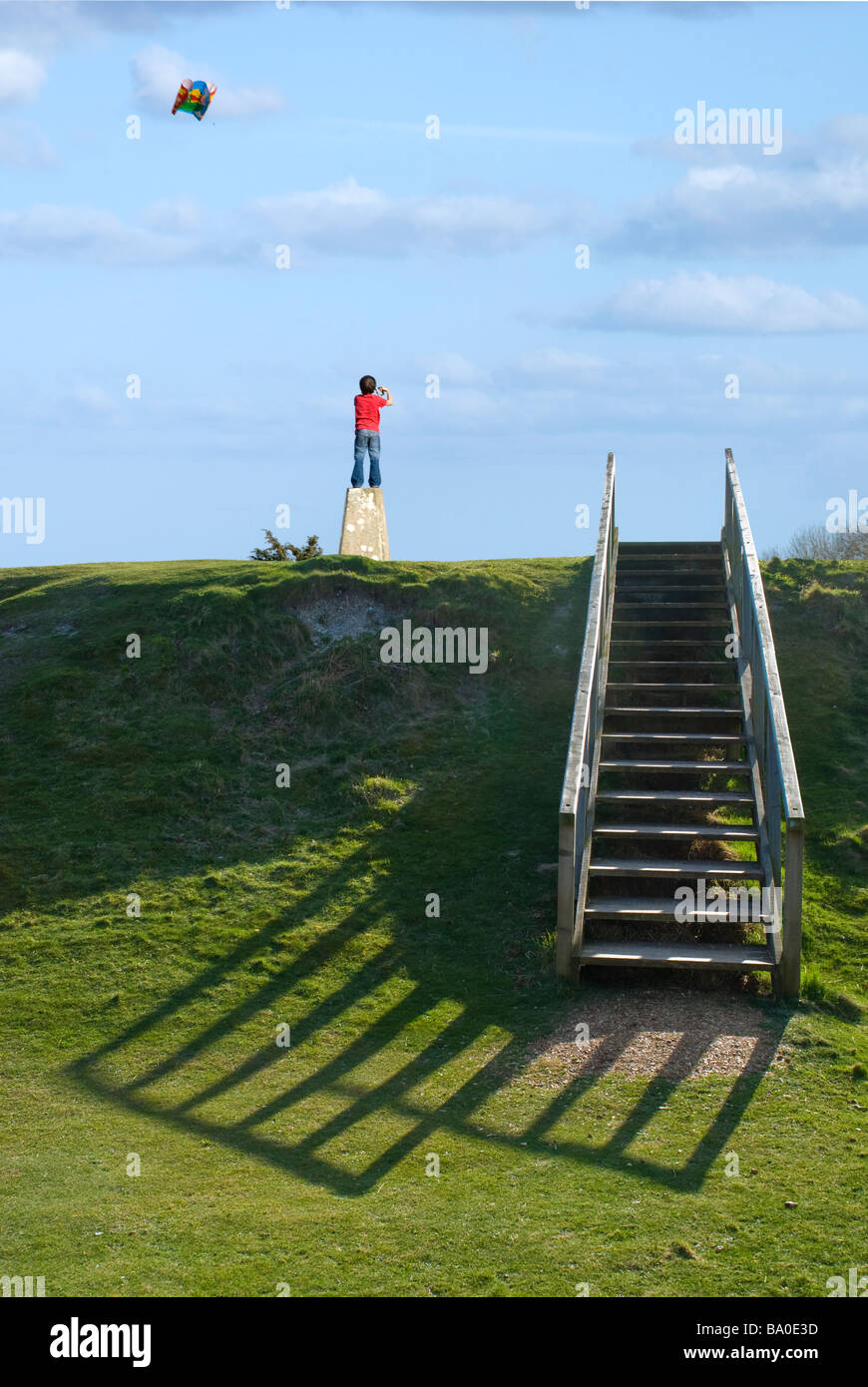 Junge einen Drachen fliegen Stand auf einer Triangulation [Trig] Punkt mit hölzernen Stufen zum Hügel top.danebury Ringe, Hampshire. Stockfoto