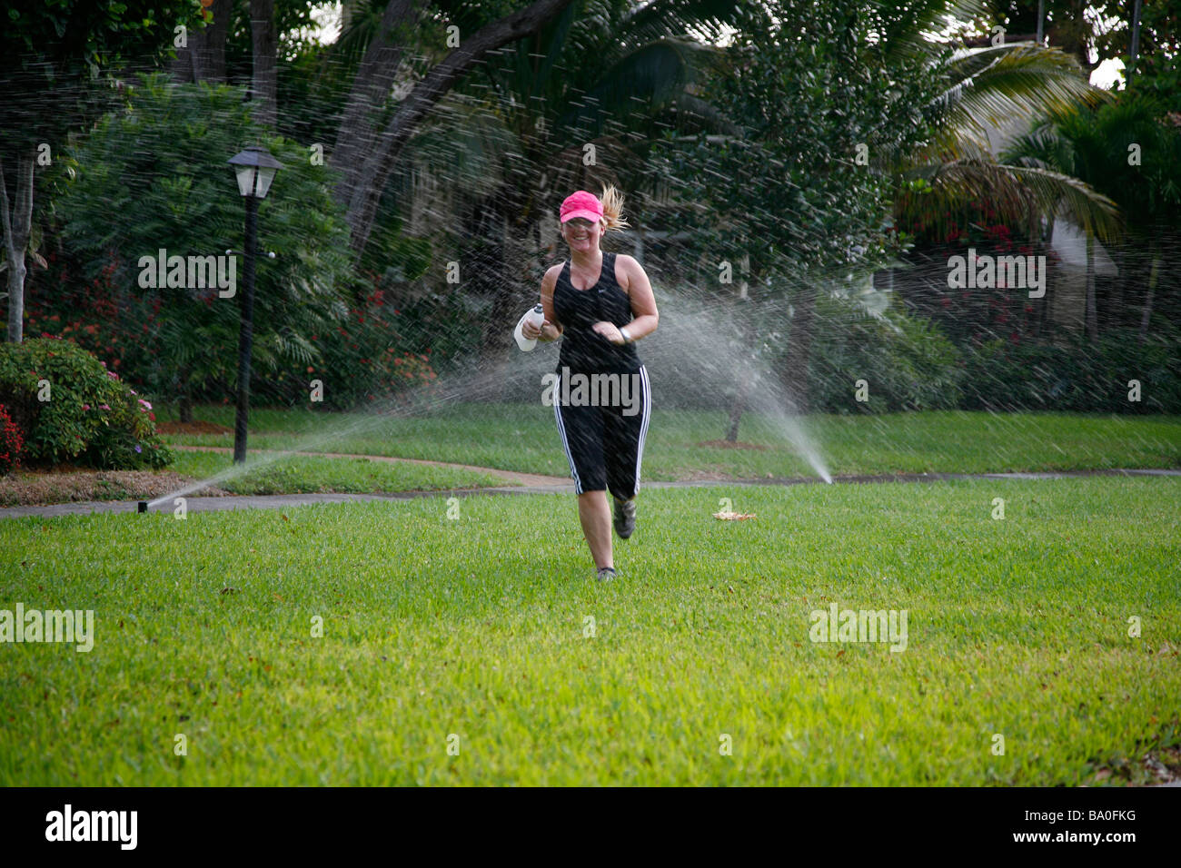 junge Frau läuft durch Sprinkler System um sich abzukühlen Stockfoto