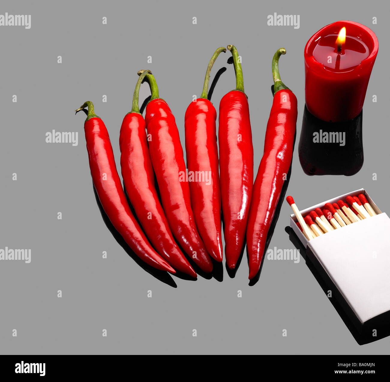 frische rote Chilischoten mit Streichhölzern und brennende rote Kerze über graue reflektierende Oberfläche Stockfoto
