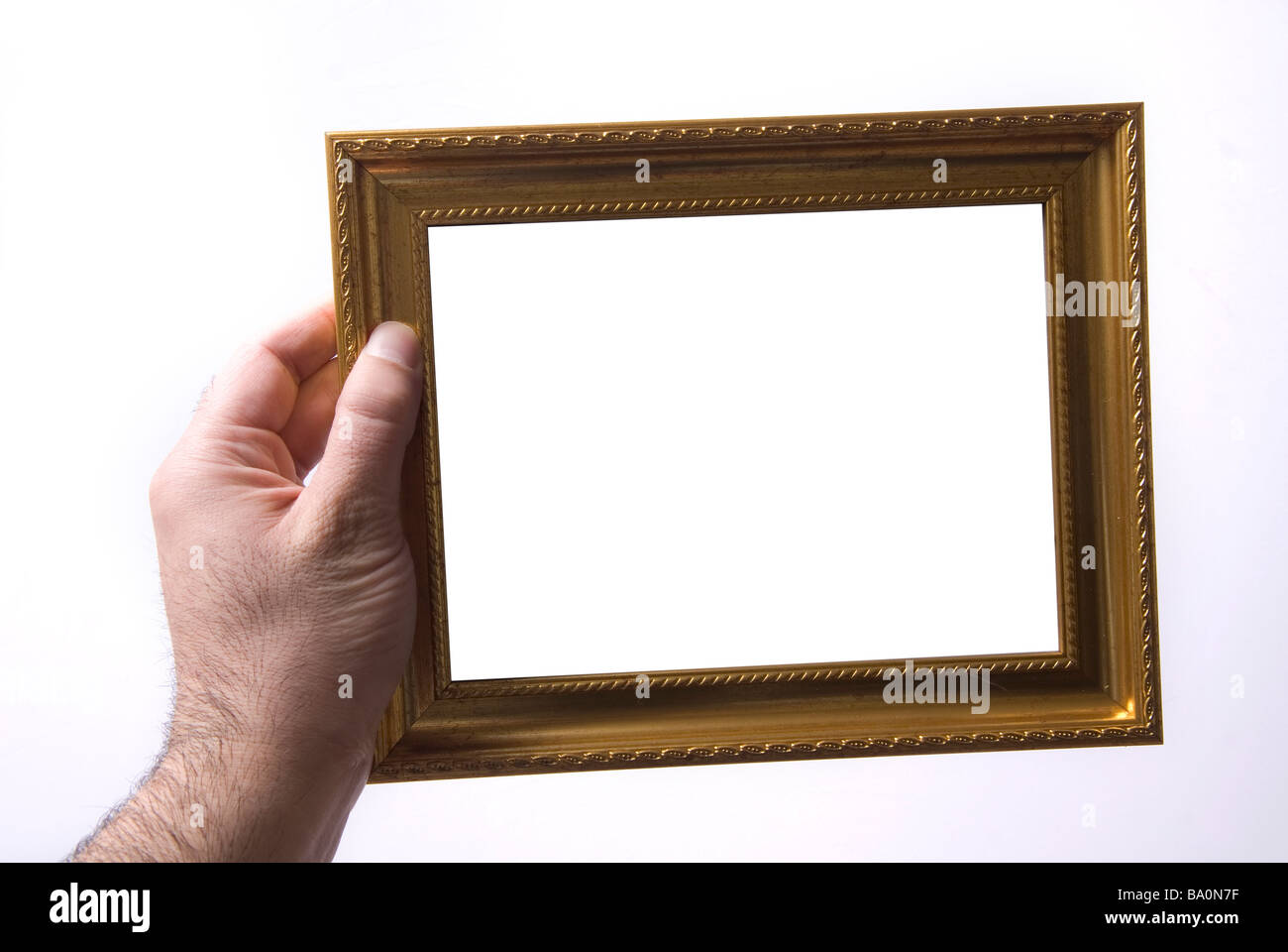 Hand, die einen goldenen Bilderrahmen vor einem weißen Hintergrund Stockfoto