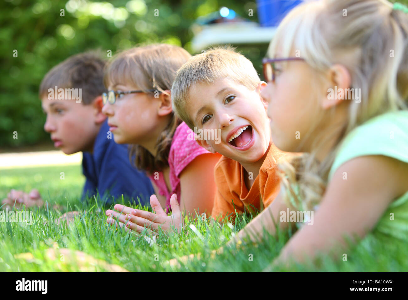 Gruppe von Kindern, die Verlegung in Rasen, ein Junge sieht in die Kamera Stockfoto