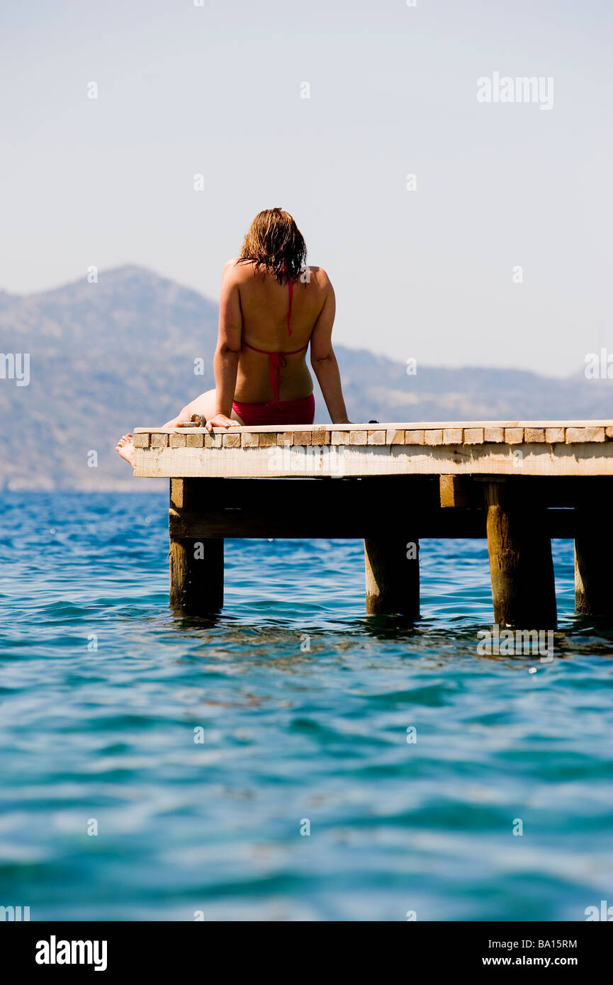 Eine junge Frau sitzt auf einem Steg mit Blick auf das Meer Stockfoto