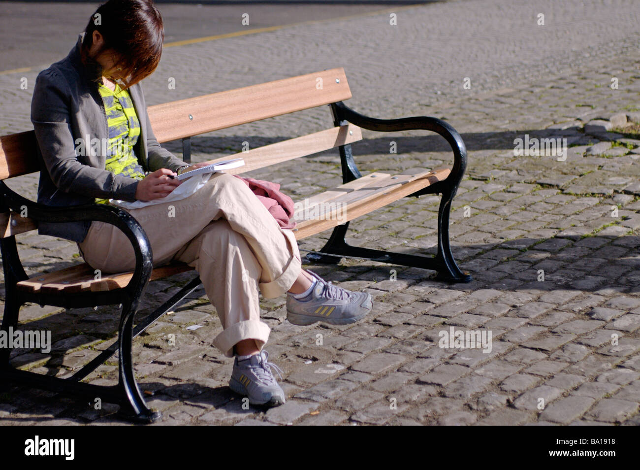 Frau sitzt alleine auf Parkbank mit dem Kopf nach unten lesen Stockfoto