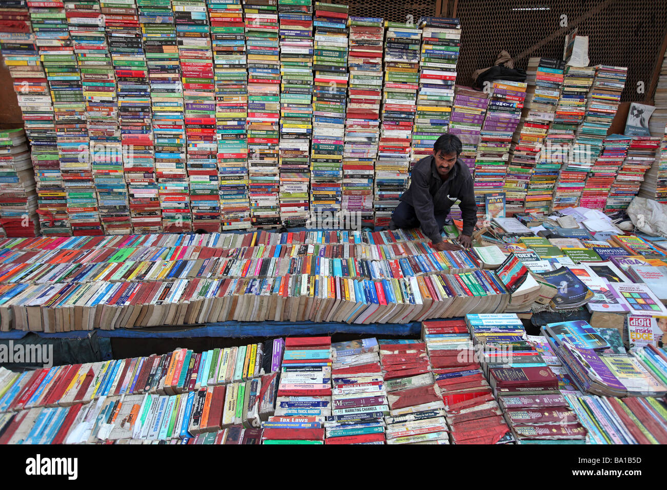 Ein Kreditor in Old Delhi Sonntag Buchmarkt ist umgeben mit Lesestoff auf seiner Straßenseite Stall. Stockfoto