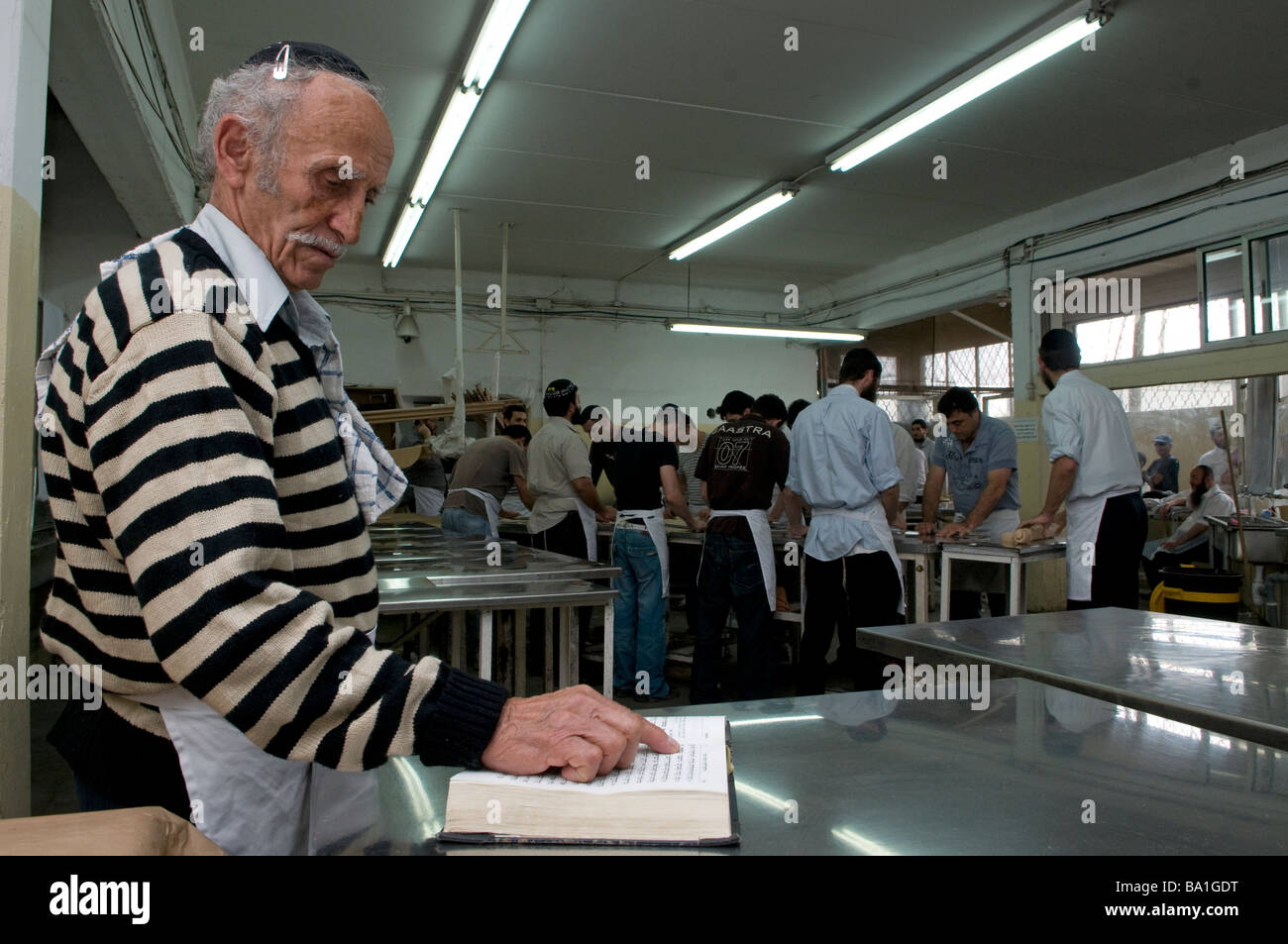 Ein religiöser jude betet, während andere Juden Matzot traditionell vorbereiten Ungesäuertes Brot, das am Passahfest in der Kfar Chabad Bäckerei gegessen wird Zentralisraelisch Stockfoto