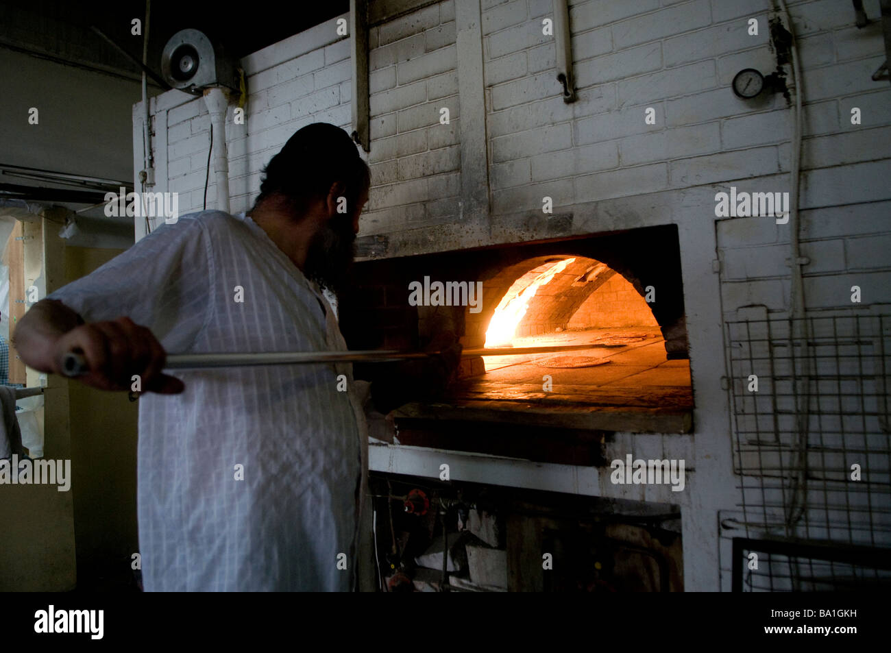 Ein religiöser Jude, der ein Matzah traditionelles handgemachtes Passah ungesäuert platziert Brot in einem Holzofen in der Bäckerei Kfar Chabad in Central Israel Stockfoto