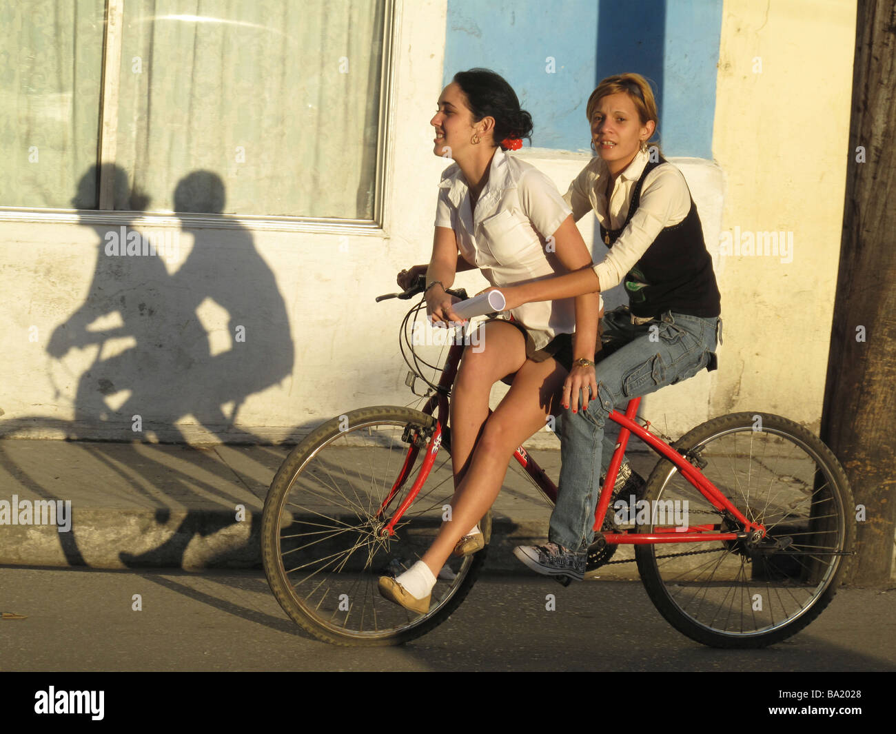Zwei Mädchen im Teenageralter auf einem roten Fahrrad Rad fahren durch die Stadt am späten Nachmittag in Sancti Spíritus, Kuba Stockfoto