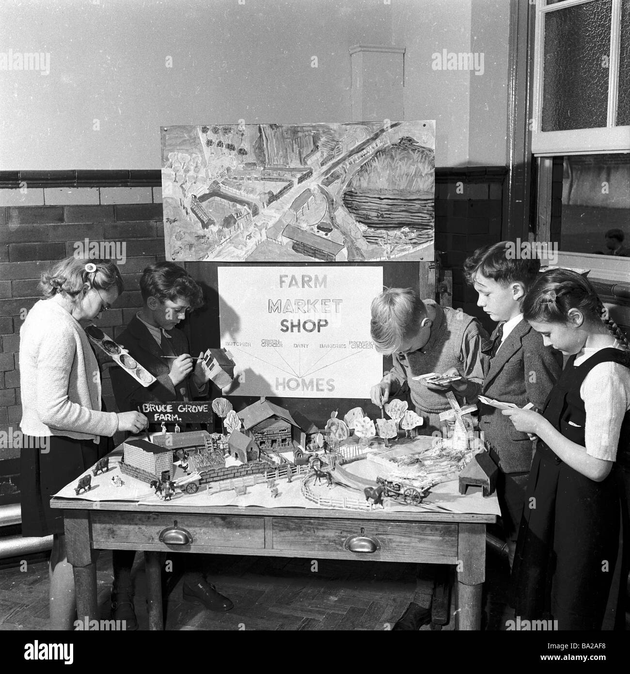 1950s, Großbritannien nach dem Krieg, Kinder in einem Klassenzimmer, die eine Modellfarm machen, mit einem Zeichen darüber, wie die angebauten Lebensmittel auf den Markt, in Geschäfte und dann in Häuser gehen Stockfoto