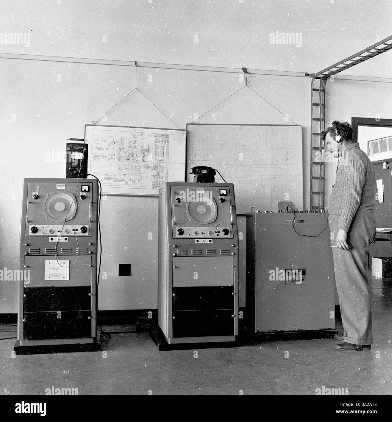 1950s, Telekommunikation, männlicher Bediener mit Kopfhörern, der neben einer Maschine von Marconi steht, einem Pionier der drahtlosen Fernkommunikation. Stockfoto