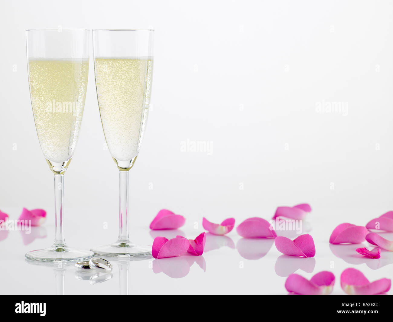 Zwei Trauringe neben Champagner-Flöten und Rosenblüten Stockfoto