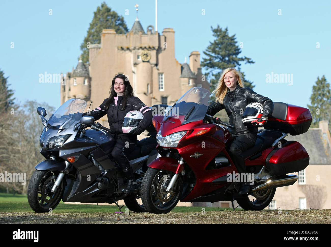 Zwei weibliche Motorradfahrer posiert mit Fahrräder tragen von Schutzkleidung an schottischen Schloss Ort Stockfoto