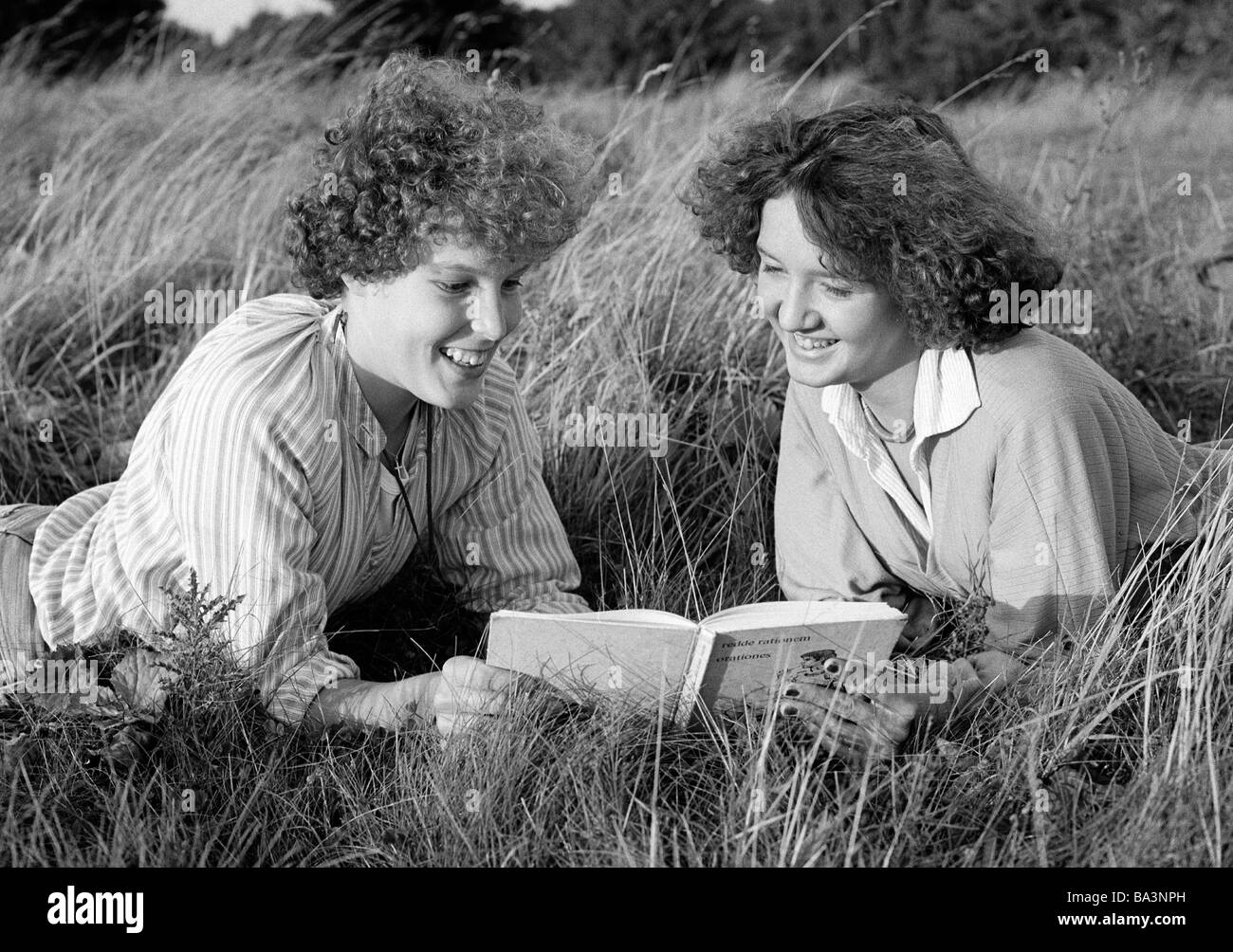70er Jahre, schwarz / weiß Foto, Menschen, zwei junge Mädchen liegen in der Wiese lesen gemeinsam in einem Buch, Bluse, Pulli, im Alter von 16 bis 20 Jahre Stockfoto