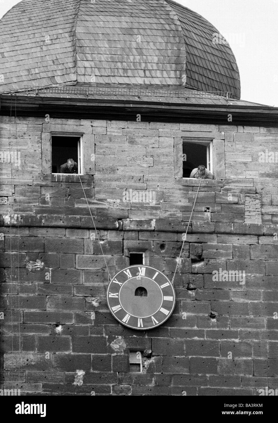 Achtziger Jahre, schwarz / weiß Foto, Menschen, Humor, Wiedergutmachung eine Turmuhr auf einen Kirchturm, zwei Männer aus verschiedenen Fenstern rechtfertigen das Ziffernblatt der Turmuhr mit einem Seil Stockfoto