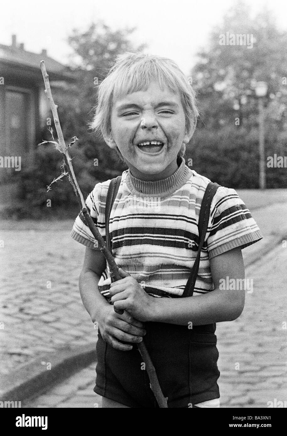 Der siebziger Jahre, schwarz / weiß Foto, Menschen, Kinder, wenig junge, Porträt, Straßenkind, schmutzig, unkemptly, hält einen Stock in der Hand und macht ein Gesicht, im Alter von 4 bis 6 Jahre Stockfoto