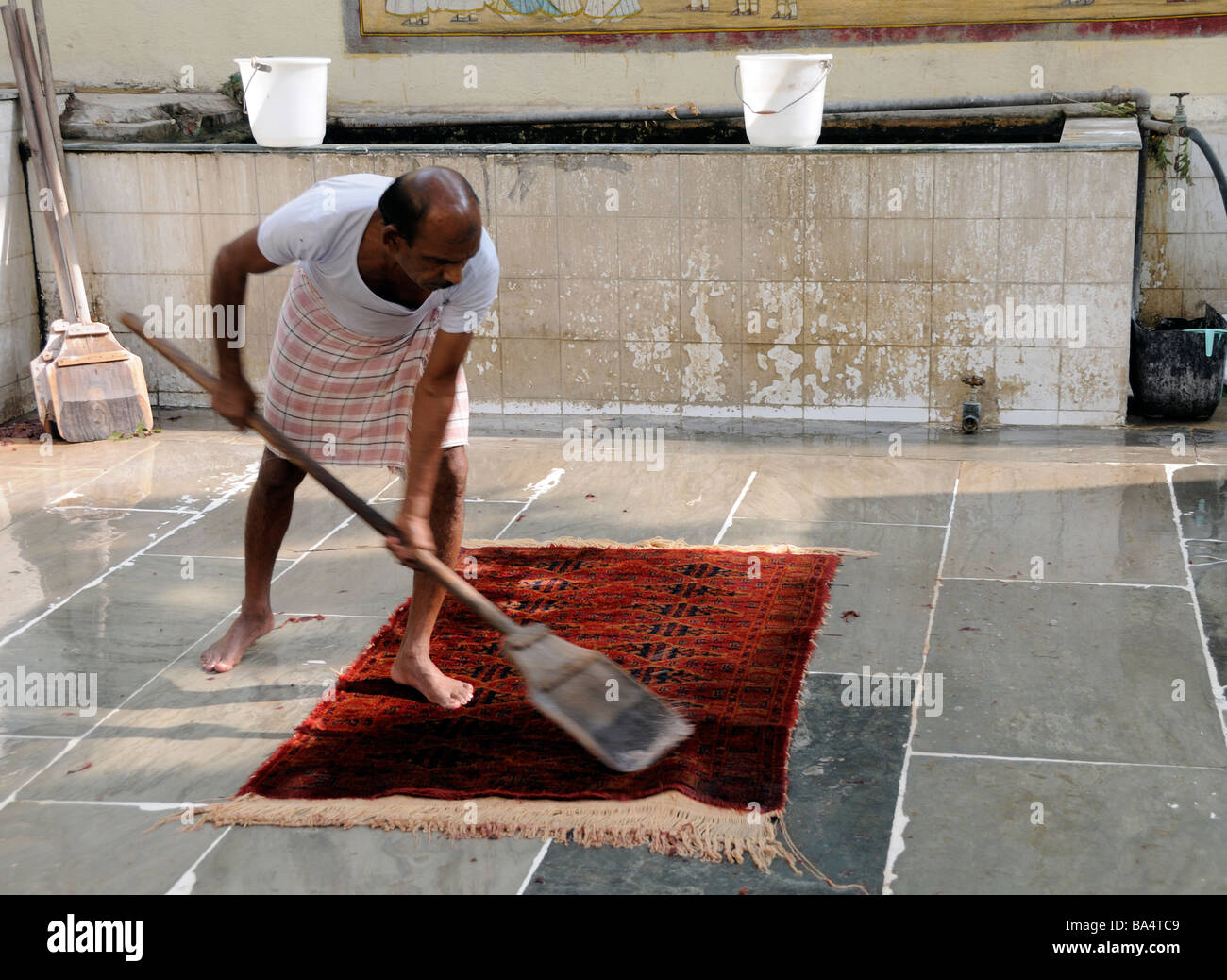 Ein Arbeiter in einer Hand-made Teppich-Genossenschaft in Jaipur wäscht energisch einen neuen handgeknüpfter Teppich mit Wasser und einem hölzernen Paddel Stockfoto