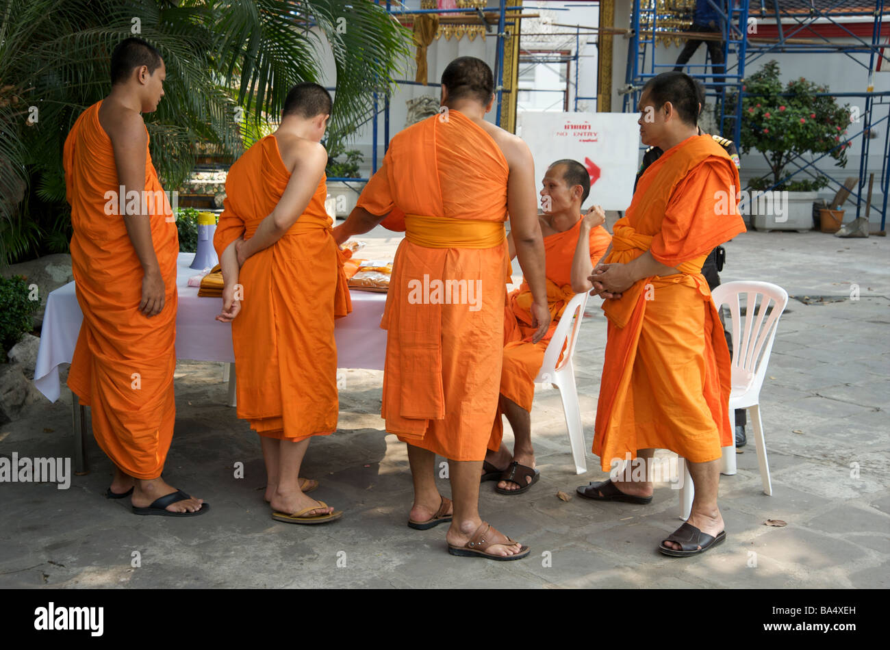 Fünf buddhistische Mönche stehen an, um Safranroben für Opfergaben im Wat Pho Bangkok Thailand auszuwählen Stockfoto