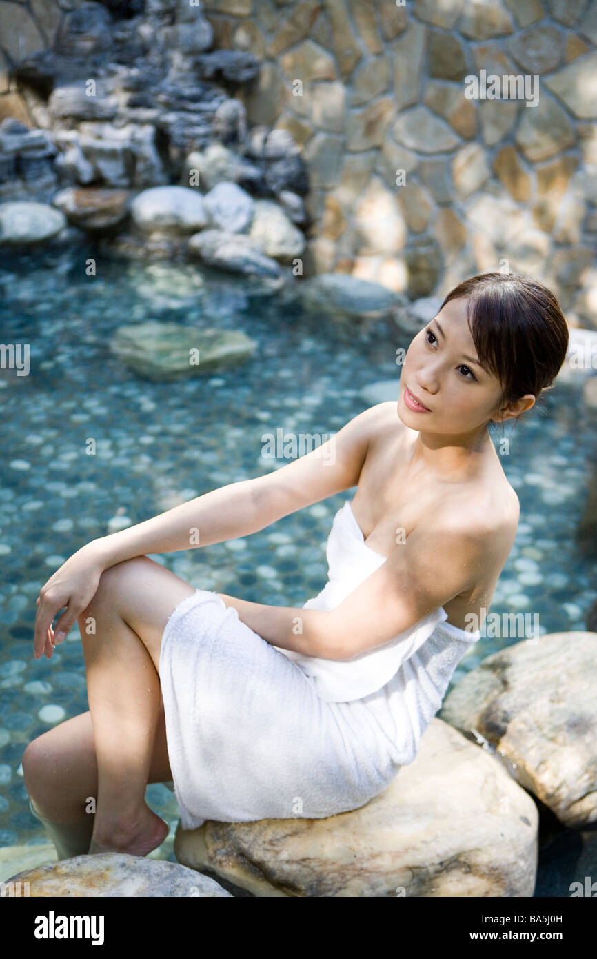 Junge Frau im Badehandtuch sitzen auf Felsen Therme Seitenansicht Stockfoto