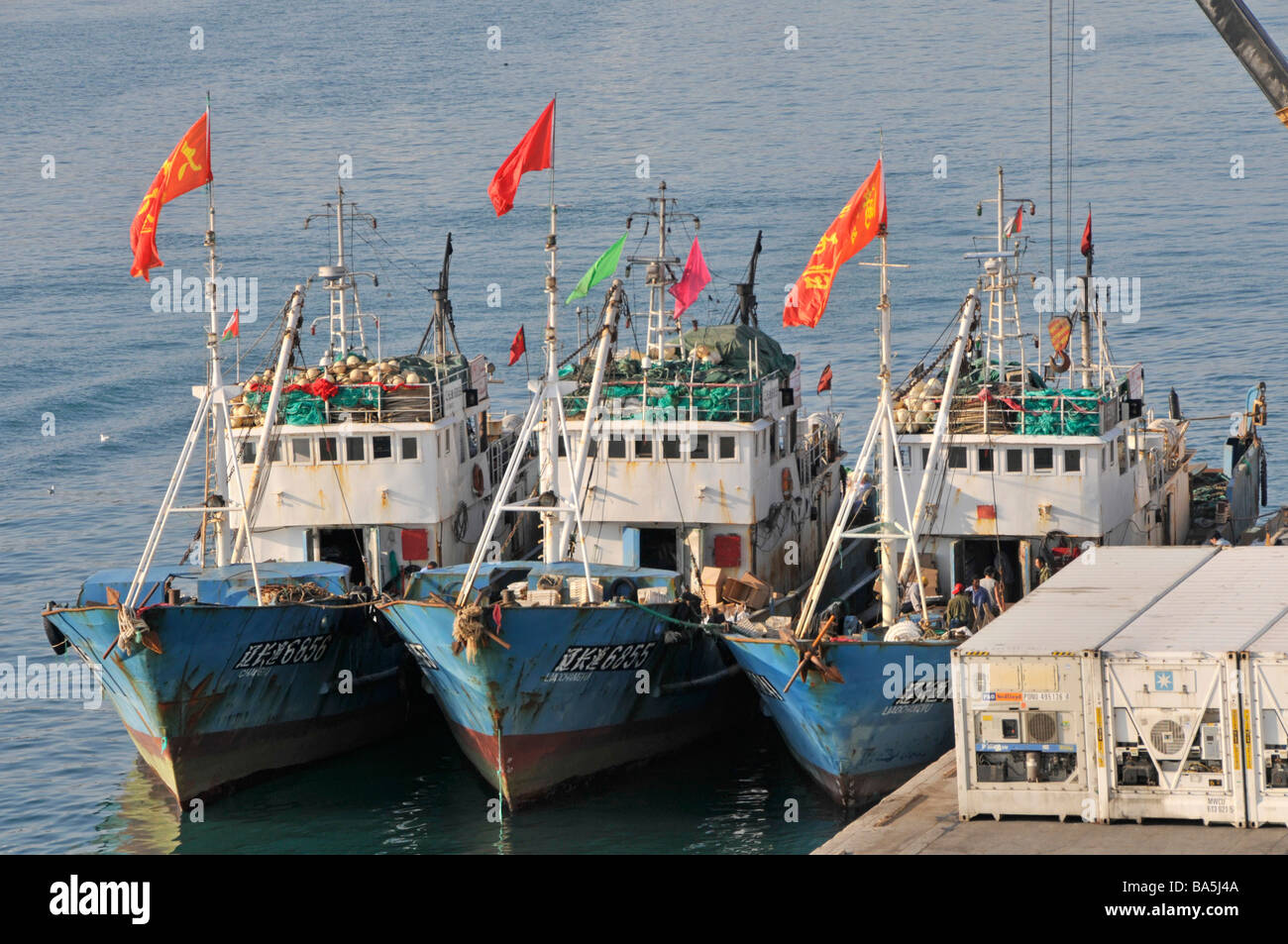 Die Seeleute bei der Arbeit auf der kleinen Flotte drei neben identisch Fischerboote am Hafen von Port Sultan Qaboos mit Kühlhaus Container bei Muttrah Muscat Oman Stockfoto