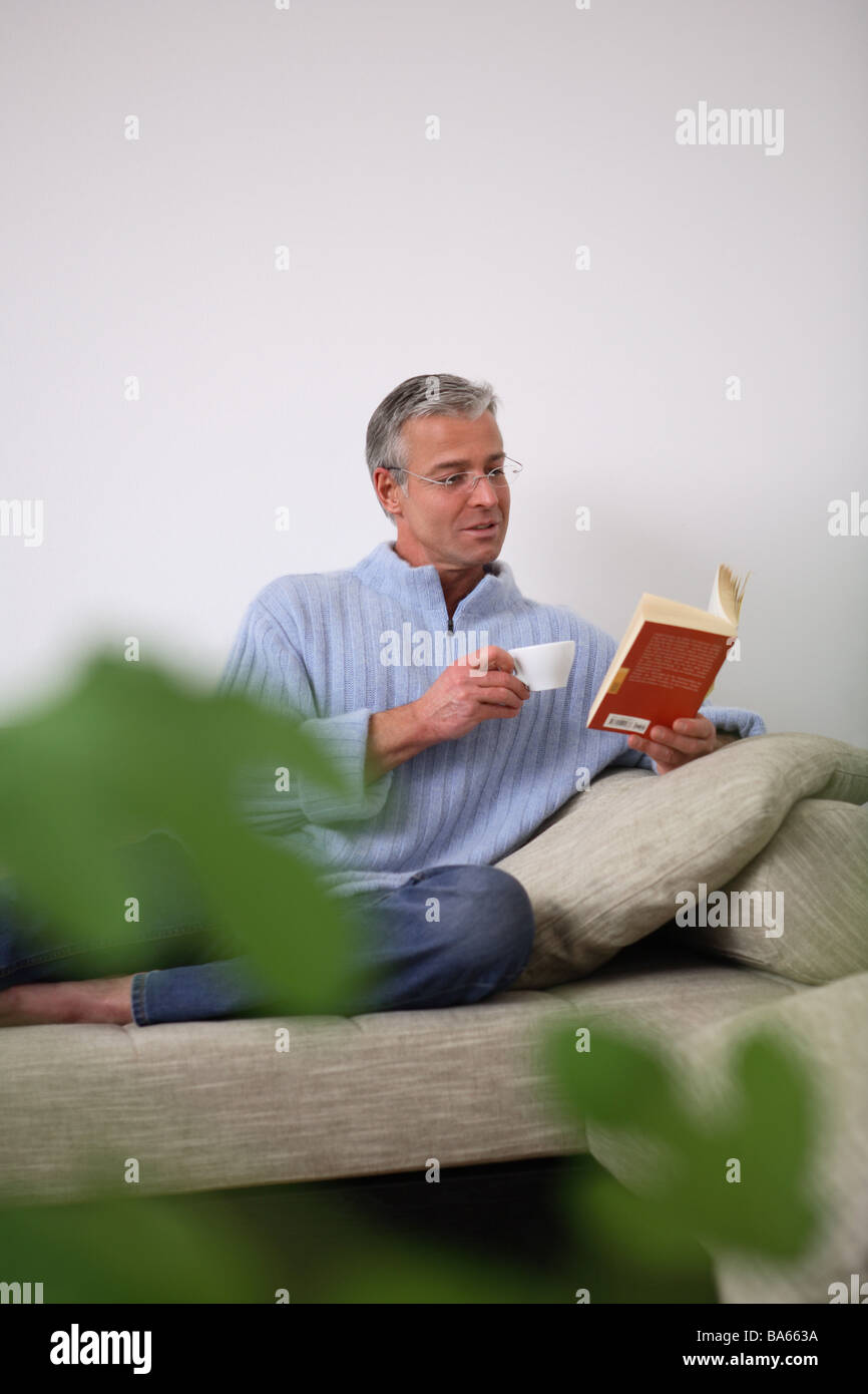 Wohnzimmer Sofa Mann Buch Cup lesen Pflanze Unschärfe Menschen 30-40 Jahren 40-50 Jahre Brille Lesebrille Brillen-Träger Stockfoto