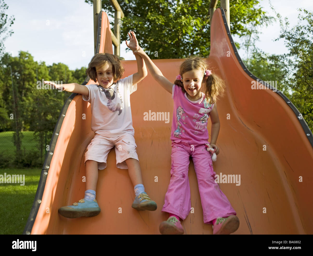 Zwei Mädchen Rutschbahn spielt fröhlich Serie Leute Rutschen Kinder Freunde Schwestern Zwillinge Garten Rutschen Kindheit Freude Stockfoto