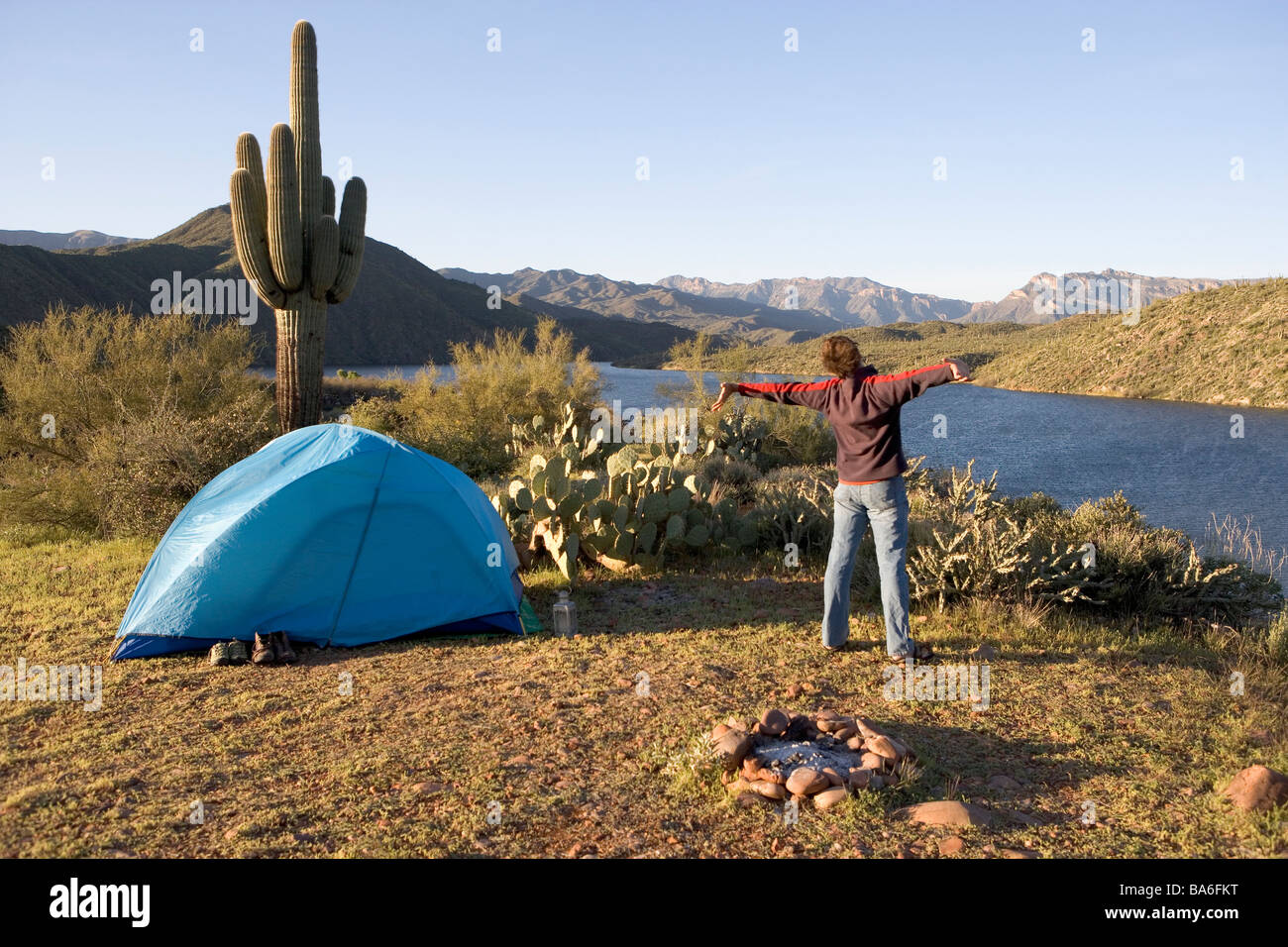 Ein Mann gähnt und erstreckt sich beim camping allein bei Sonnenaufgang auf einer Klippe mit Blick auf Apache Lake Arizona Stockfoto