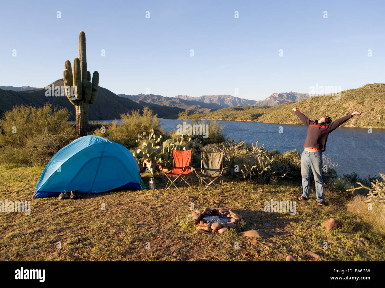 Ein Mann gähnt und erstreckt sich beim camping allein bei Sonnenaufgang auf einer Klippe mit Blick auf Apache Lake Arizona Stockfoto