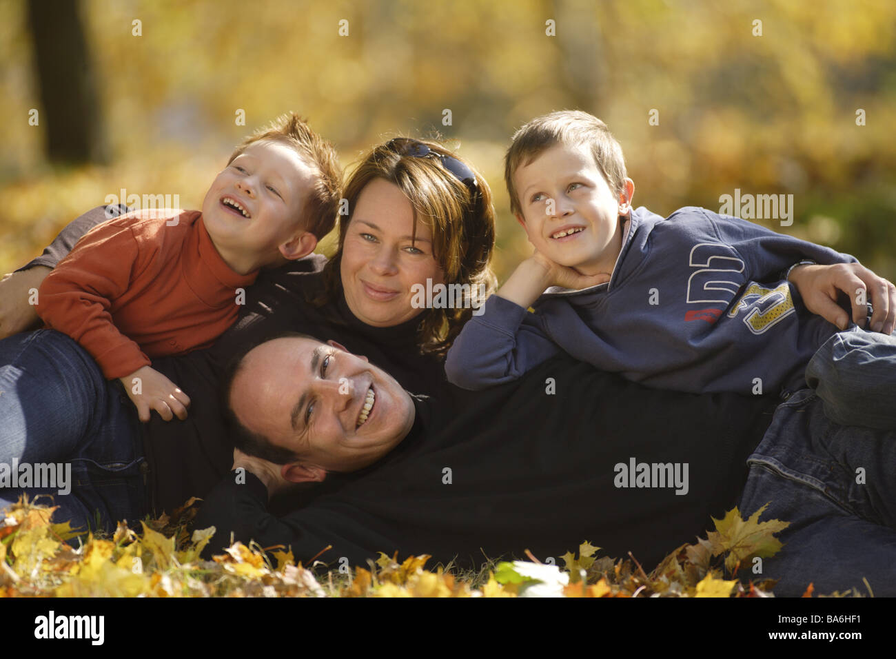 Familie Herbstlaub Lügen lacht fröhlich Blick Kamera Erwachsene Eltern Kinder jungen Söhne außerhalb Herbst Laub fallen Blätter Stockfoto