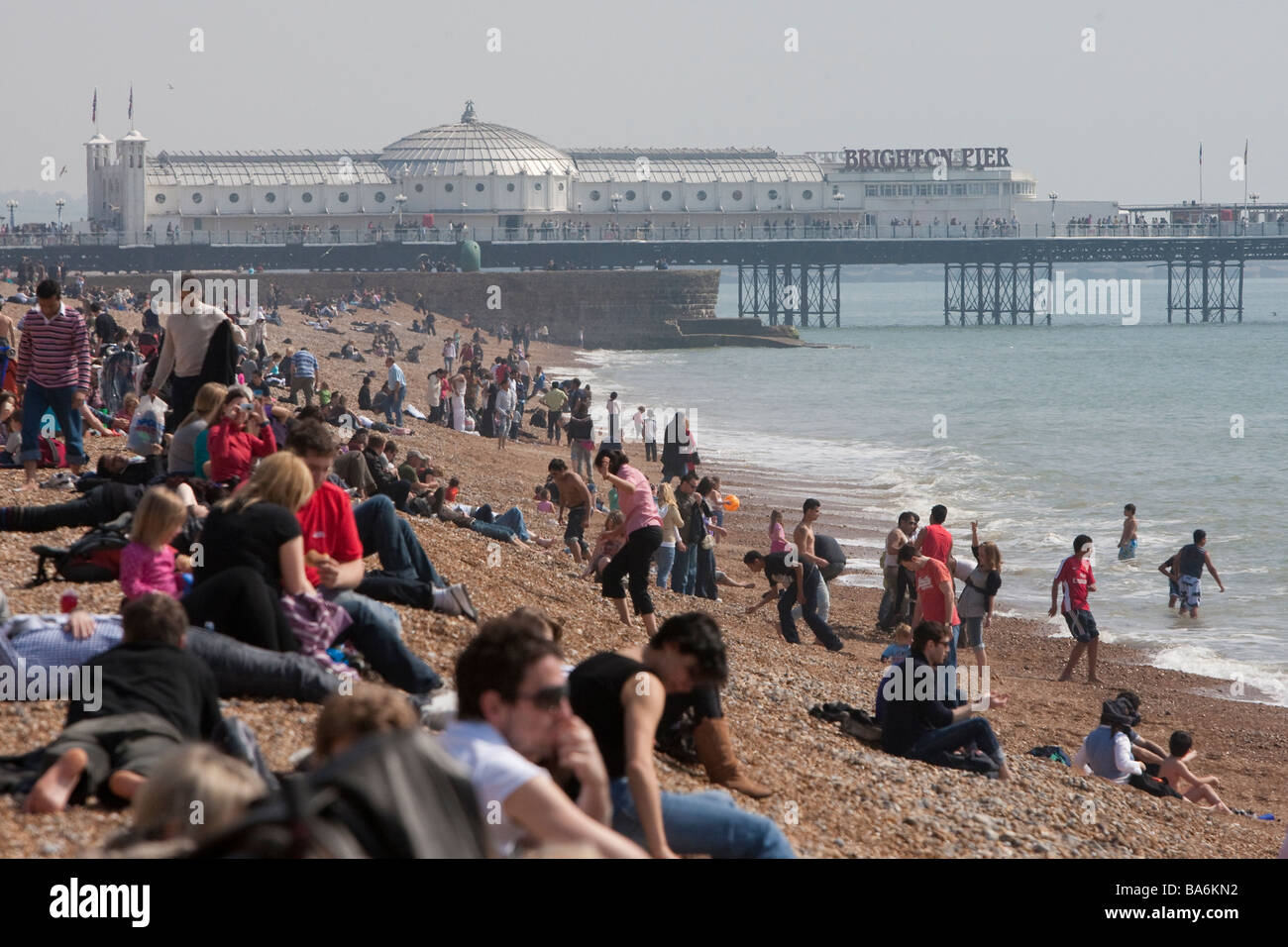 Urlauber am Strand von Brighton, Palace Pier im Hintergrund, Brighton, Ostern Bank Holiday Montag Stockfoto