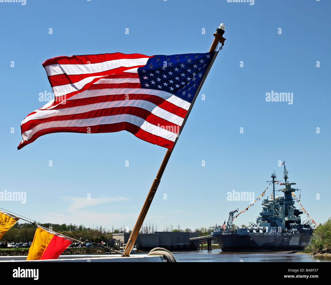 Amerikanische Flagge alte Herrlichkeit Sternenbanner fließt am Fluss mit Schlachtschiff USS North Carolina im Hintergrund blauer Himmel Stockfoto