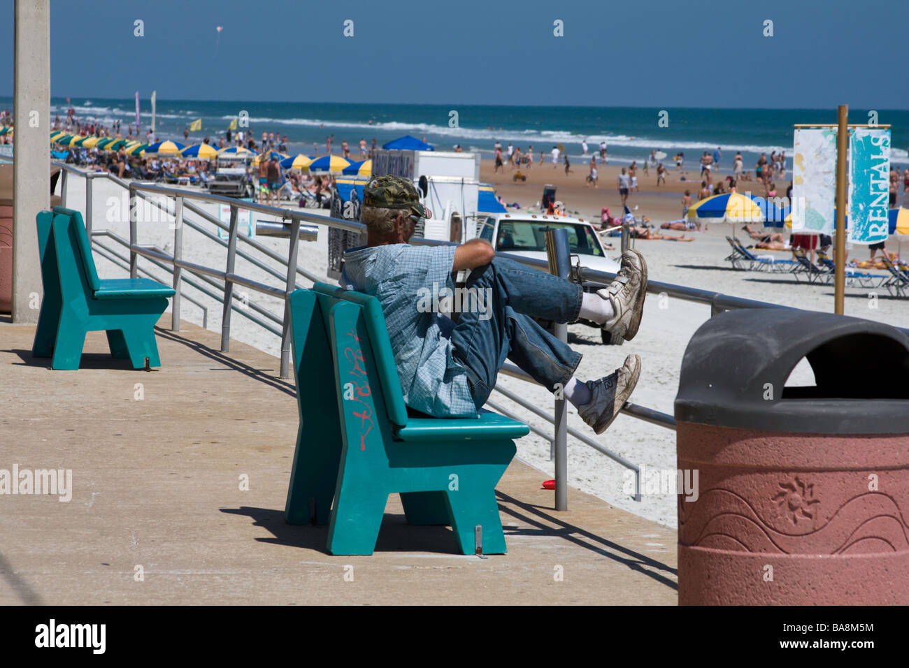 Transiente Obdachloser sitzt an einem Strand an einem touristischen Ort gefragt, woher seine nächste Mahlzeit kommen soll Stockfoto