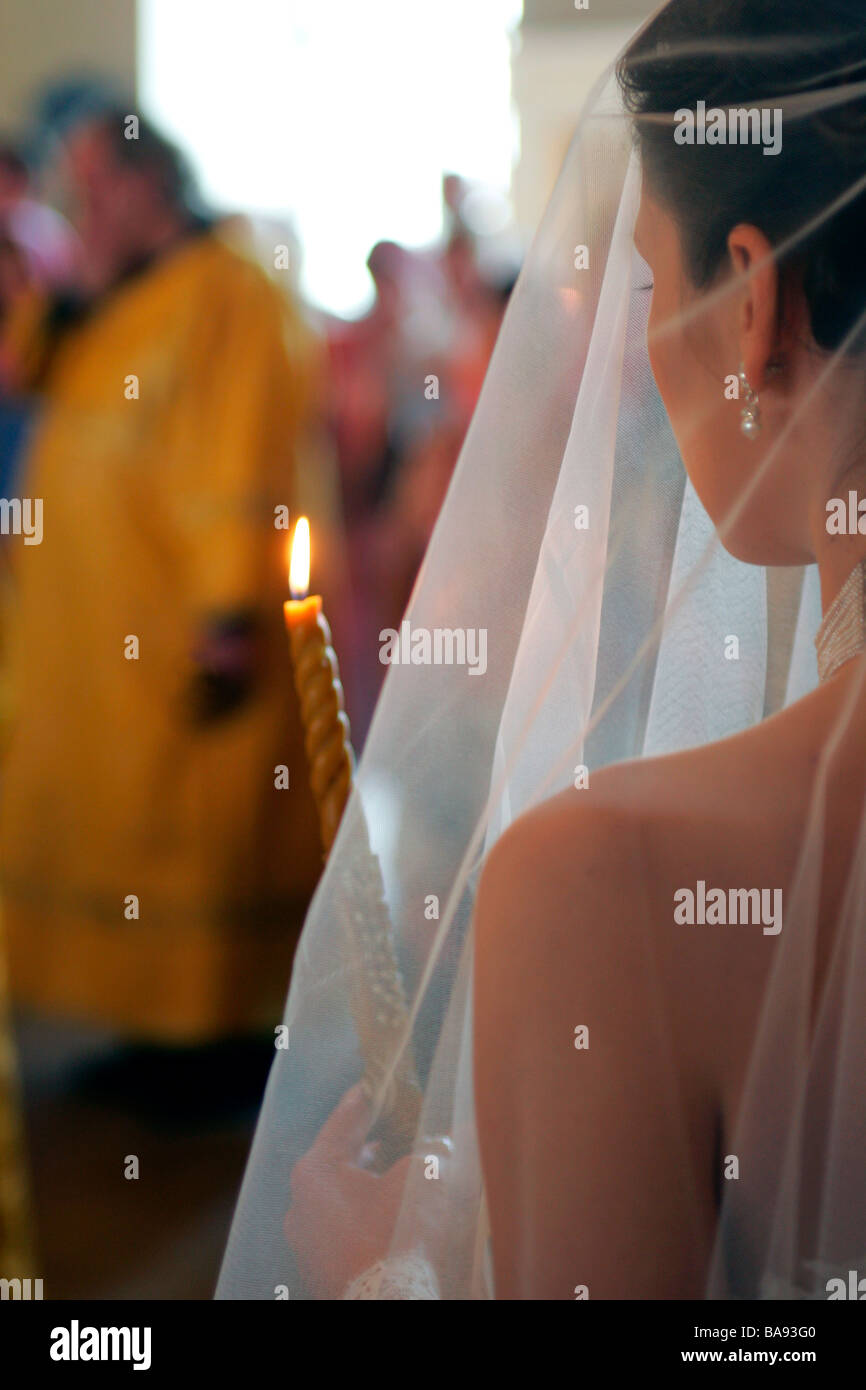 Rückansicht des verschleierten Braut hält beleuchtete Kerze in der Kirche Stockfoto
